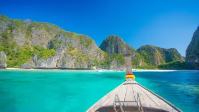 Boat on turquoise sea facing tropical cliffs